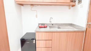 A compact kitchen with a sink, countertop, and wooden cabinets. - Compact And Restful Studio At Pavilion Permata Apartment (Surabaya)