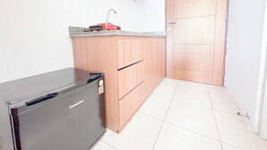A compact kitchen with a refrigerator, wooden cabinets, and a tiled floor. - Compact And Restful Studio At Pavilion Permata Apartment (Surabaya)
