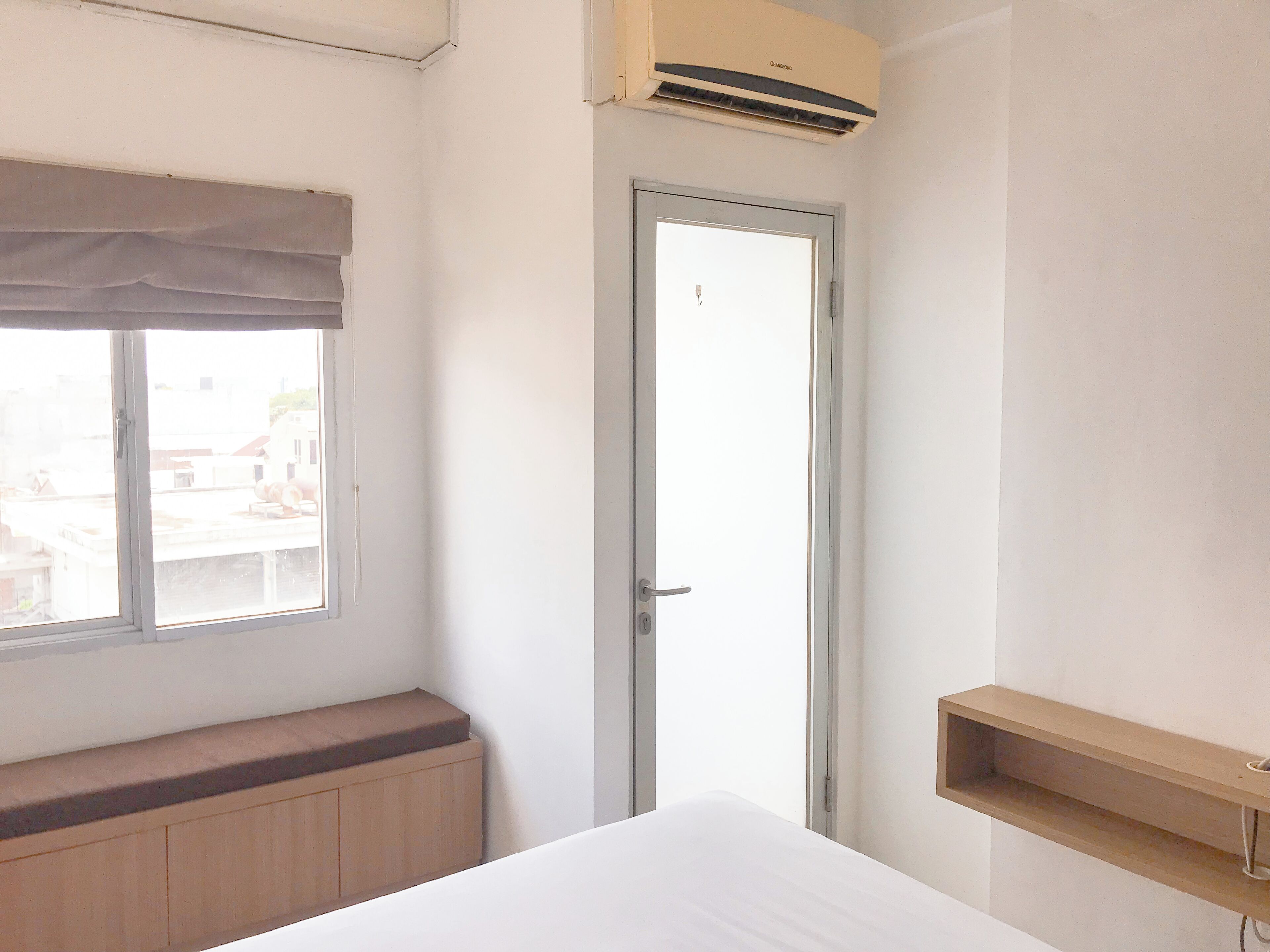 Un dormitorio con cama, ventana con cortina, puerta y aire acondicionado.