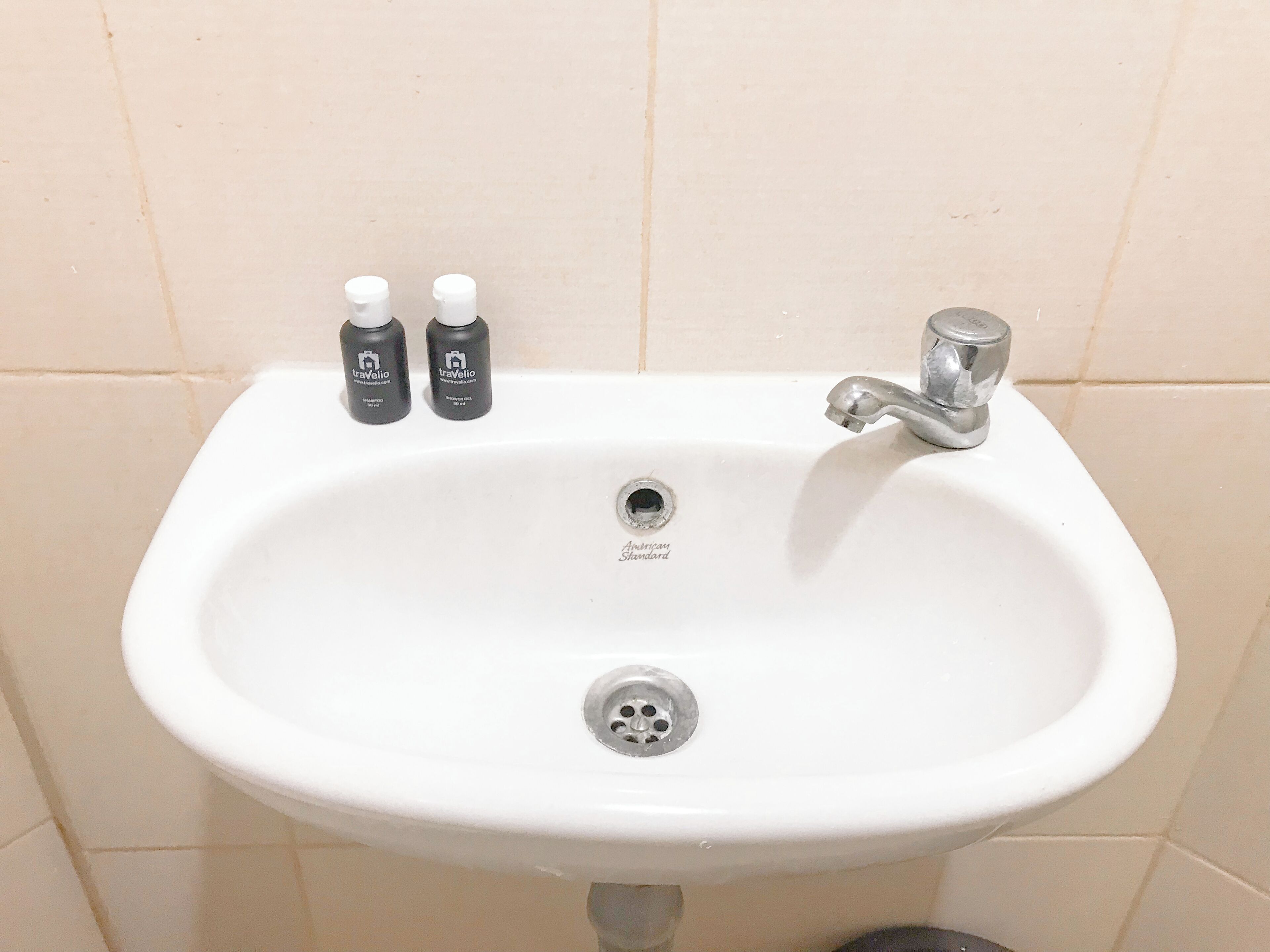 A white bathroom sink with two bottles of Travelio hand soap, a chrome faucet, and a drain.