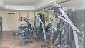 Ein Fitnessstudio mit verschiedenen Trainingsgeräten, einer Spiegelwand und Holzboden.