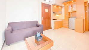 A compact living space with a sofa, a glass coffee table, and a kitchenette area.
