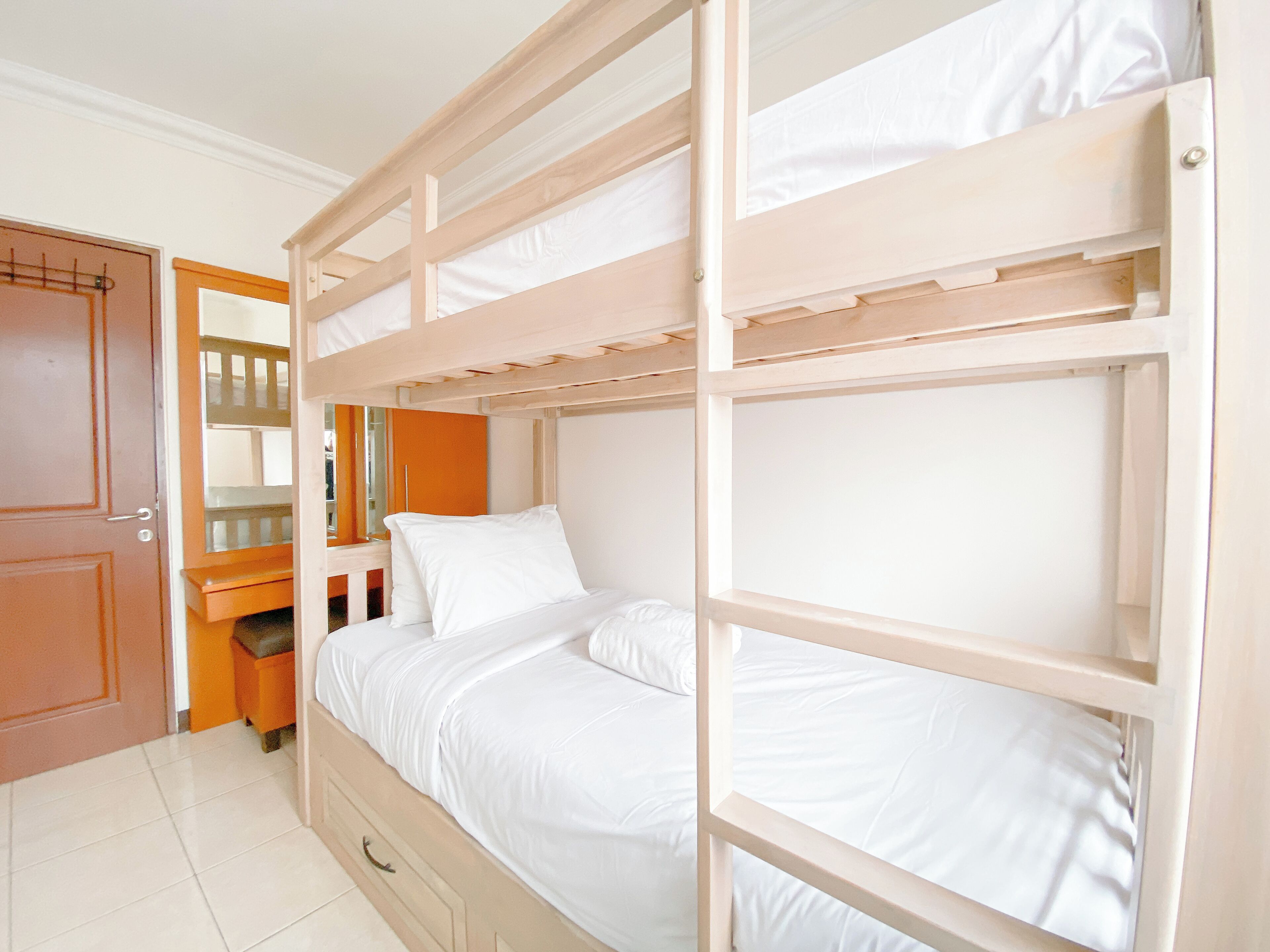 A bunk bed room with a wooden frame, white bedding, and a wooden door.