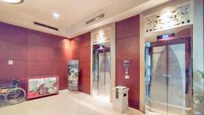 A modern hotel lobby with elevators, a wheelchair, and a small trash bin.