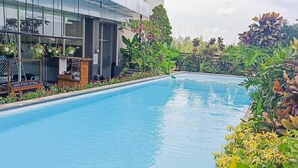 A swimming pool with a sign for a live food stall, surrounded by lush greenery and a modern building in the background.