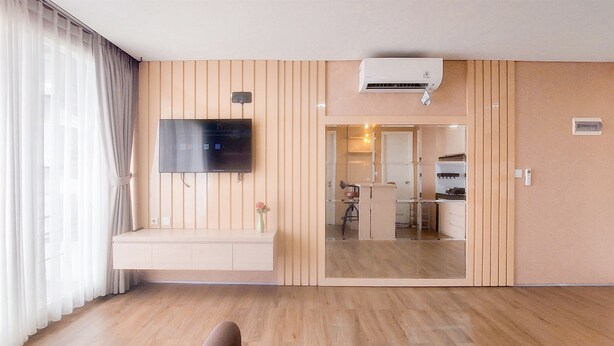 A modern living room with a flat-screen TV mounted on the wall, wooden flooring, and a sliding glass door leading to a kitchen area.