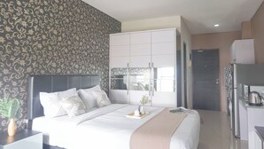 Una habitación de hotel moderna con una cama grande, un armario, una pequeña kitchenette y un baño visible a través de una puerta.