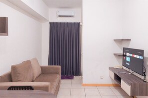 Una sala de estar con un sofá, un televisor de pantalla plana, una mesa de centro y una mesita con el control remoto.