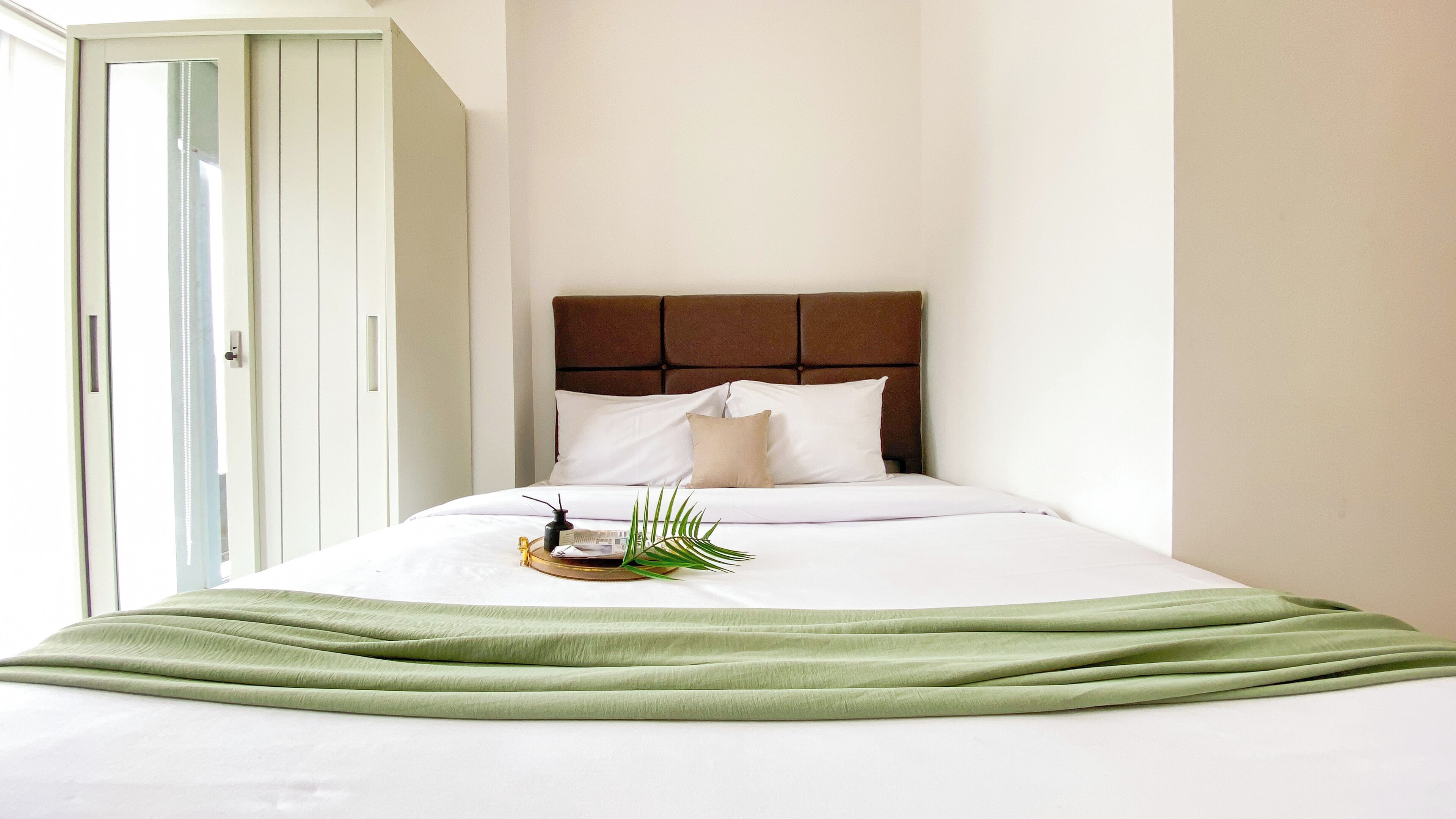 A neatly made bed with a brown headboard, white bedding, and a green throw blanket.