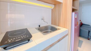Una cocina moderna con baldosas blancas, un lavamanos de acero inoxidable, una cocina de inducción negra y un refrigerador rosa.