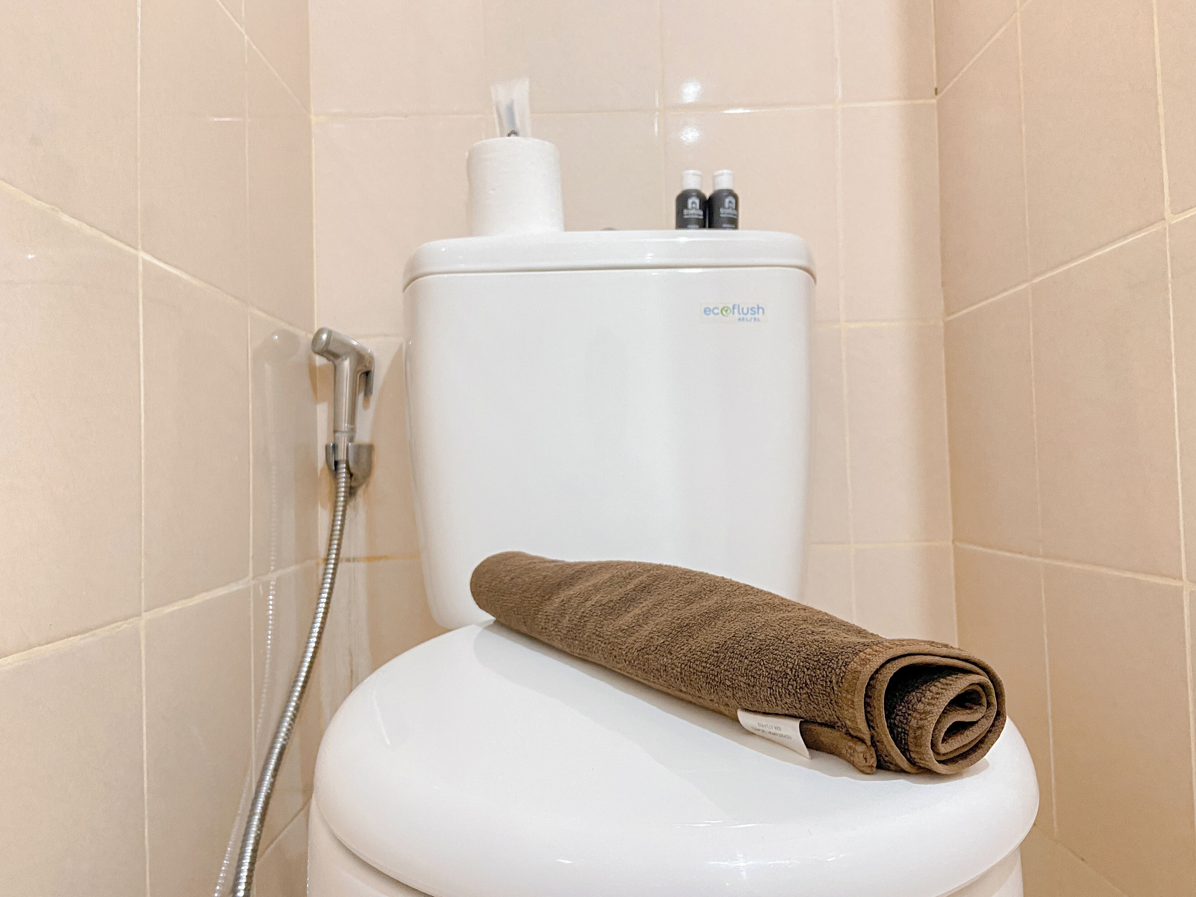 A bathroom with a white toilet, a shower head, and a towel on the toilet seat.