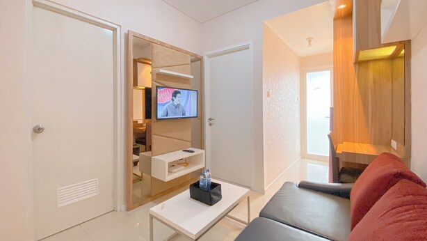 Una sala moderna con un televisor de pantalla plana montado en la pared, una mesa de centro blanca, un sofá gris y un cojín rojo.