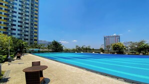 Une piscine dotée d’une terrasse carrelée, entourée de verdure et d’immeubles imposants.