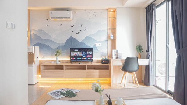 A modern hotel room with a bed, a desk with a computer, a chair, and a large window with curtains. - Cozy And Spacious Studio At Daan Mogot City Apartment (Jakarta)