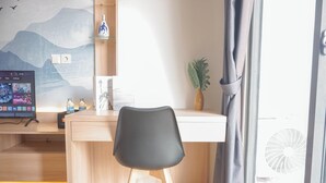 A modern room with a wooden desk, a black chair, a small plant, and a wall-mounted shelf with decorative items. - Cozy And Spacious Studio At Daan Mogot City Apartment (Jakarta)