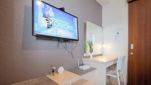 A modern hotel room with a flat-screen TV mounted on the wall, a white desk with a laptop, a white chair, and a wooden door.