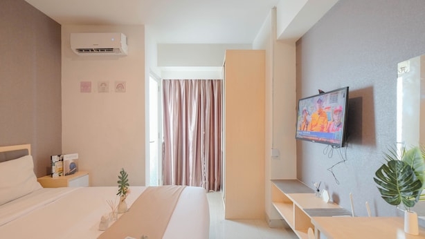 A modern hotel room with a bed, bedside table, TV, and a desk with a chair.