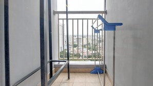 A balcony with a metal railing, a blue chair, and a mop leaning against the wall. - Tranquil Space 1Br Apartment At Podomoro City Deli Medan (Medan)