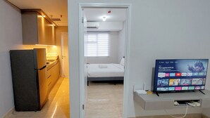 A compact hotel room with a kitchenette, a bed, and a TV displaying a streaming service interface. - Tranquil Space 1Br Apartment At Podomoro City Deli Medan (Medan)