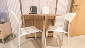 A small room with a wooden table, two white chairs, a black mug, and a white appliance. - Marvelous And Cozy 2Br At Meikarta Apartment (Cikarang)