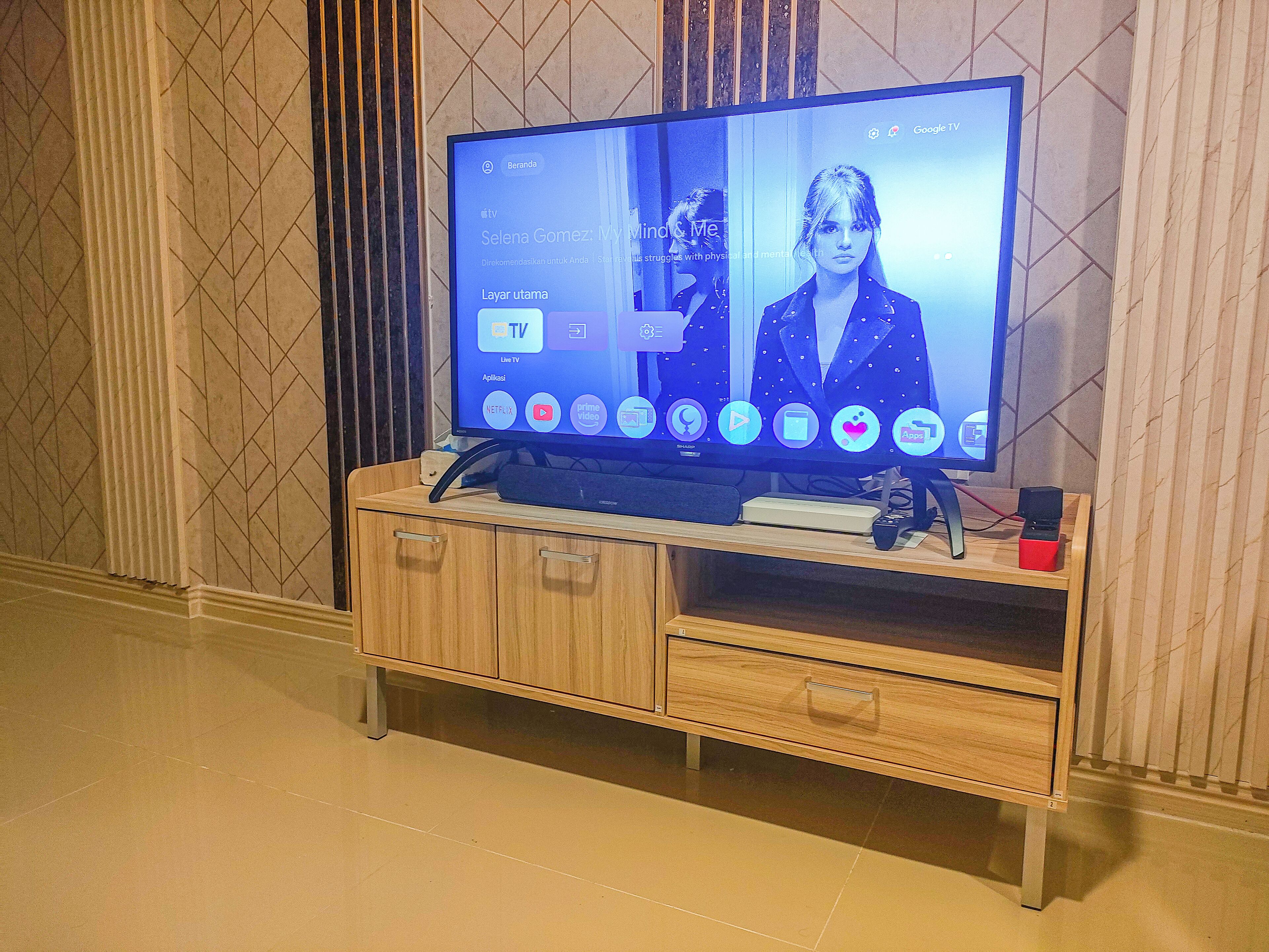 A flat-screen TV on a wooden TV stand with a remote control and a book beside it.