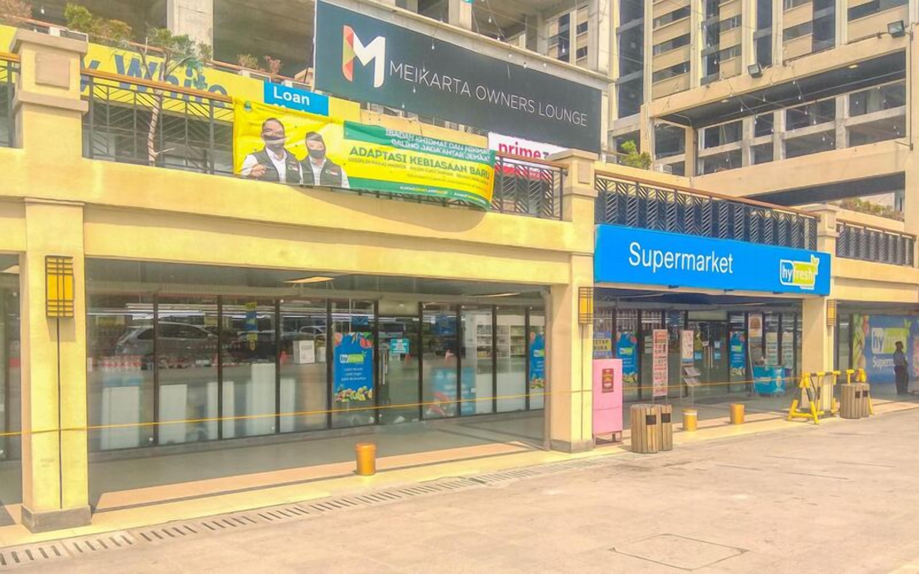 A building with a 'Supermarket' sign, a 'Loan' advertisement, and a 'Meikarta Owners Lounge' sign.
