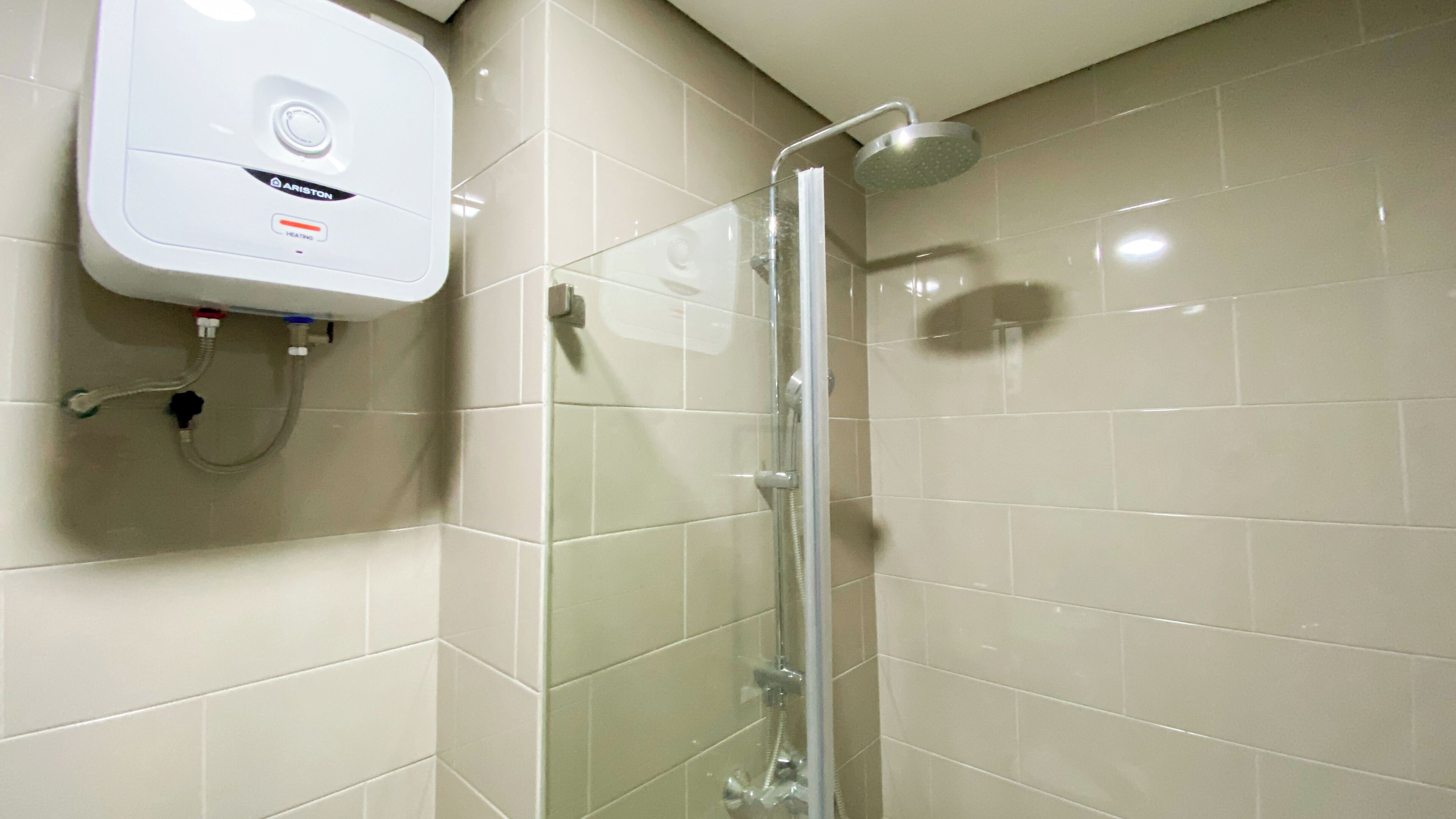 A glass-enclosed shower with a handheld showerhead, a wall-mounted heater, and a control panel labeled "ARISTON HEATING."