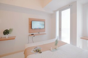 A modern hotel room with a large bed, a mounted TV, and a window providing natural light. - Homey And Cozy Studio Apartment At Tokyo Riverside Pik 2 (Teluknaga)