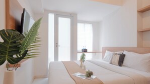 Un dormitorio moderno con cama, mesita de noche, televisor y una planta grande.
