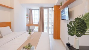 A hotel room with a bed, a TV, a desk with a computer, and a window with curtains. - Simply Look And Cozy Studio Apartment Tokyo Riverside Pik 2 (Teluknaga)