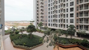 A high-rise residential building with multiple balconies, a landscaped courtyard with trees, and a view of a distant landscape. - Simply Look And Cozy Studio Apartment Tokyo Riverside Pik 2 (Teluknaga)