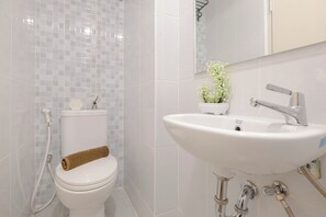 A bathroom with a white toilet, sink, and mirror, featuring a towel and a potted plant.
