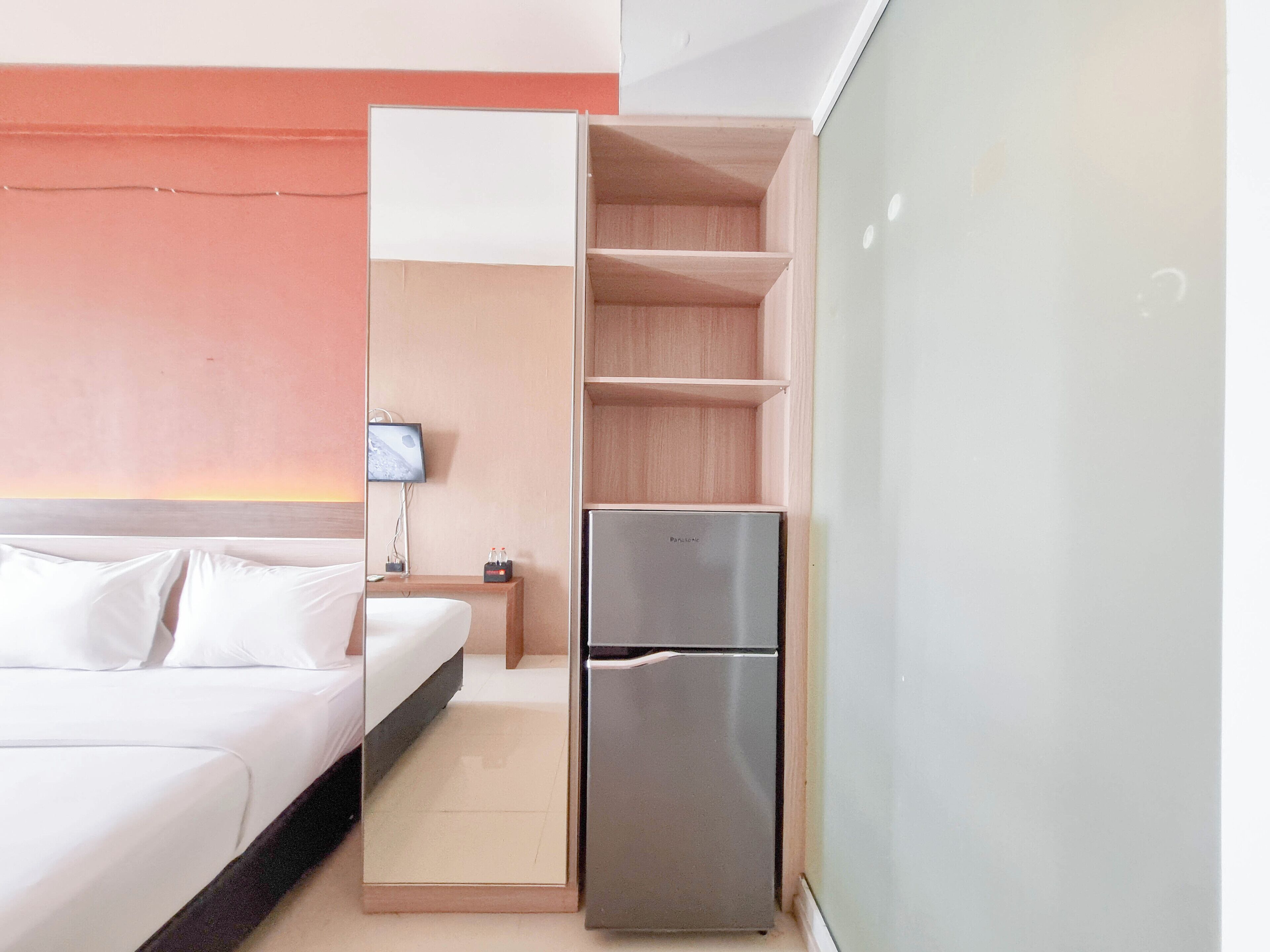 A hotel room with a bed, a minibar, a television, and a wardrobe.