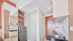 A compact kitchen with a refrigerator, a sink, and a glass door leading to a shower area. - Best Deal Studio Apartment At Vivo Yogyakarta (Depok)