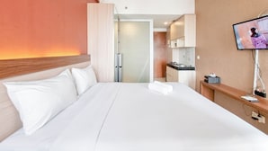 A hotel room with a bed, a TV, a desk, and a kitchenette. - Best Deal Studio Apartment At Vivo Yogyakarta (Depok)