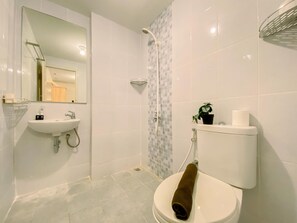 A bathroom with a sink, toilet, shower, and a towel on the toilet. - Nice View And Cozy 1Br Apartment At Tokyo Riverside Pik 2 (Teluknaga)