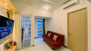 A modern living room with a red sofa, a flat-screen TV, and a sliding glass door leading to a balcony. - Nice View And Cozy 1Br Apartment At Tokyo Riverside Pik 2 (Teluknaga)