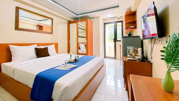 A hotel room with a large bed, a TV, a desk, and a mirror. - Comfy And Good Deal Studio At Kebagusan City Apartment (Jakarta)