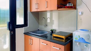 A kitchen with wooden cabinets, a black countertop, a stainless steel sink, and a water dispenser. - Comfy And Good Deal Studio At Kebagusan City Apartment (Jakarta)