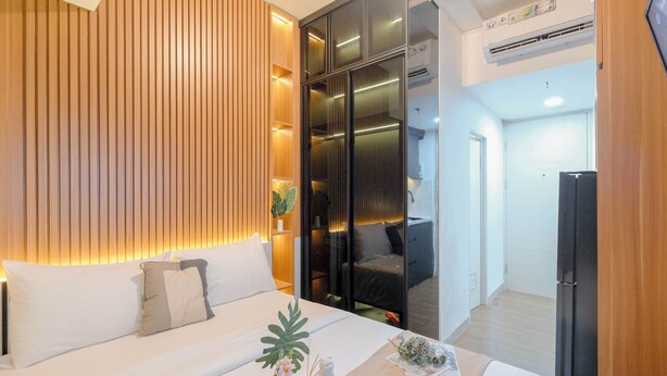 A modern hotel room with a sofa, a small table with a vase and a plant, and a sliding door leading to a balcony. - Modern Studio At Tokyo Riverside Pik 2 Apartment (Teluknaga)
