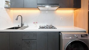 A modern kitchen with a built-in washing machine, a gas stove, and a stainless steel sink. - Modern Studio At Tokyo Riverside Pik 2 Apartment (Teluknaga)