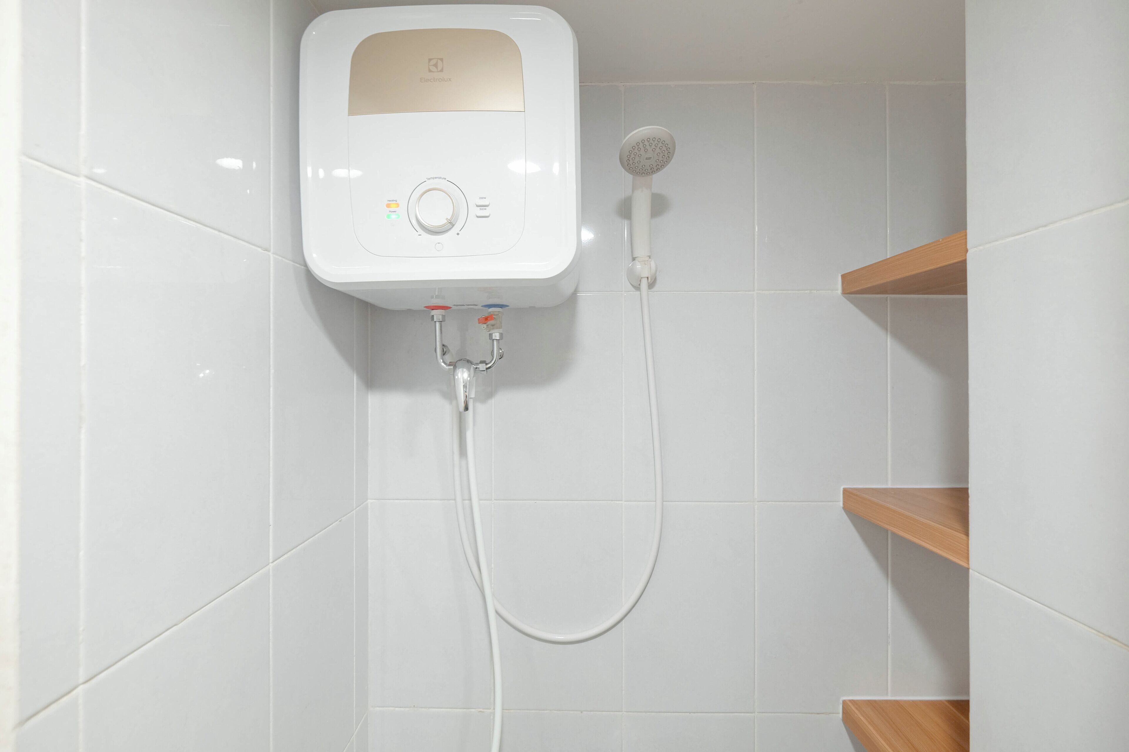 A modern bathroom with a wall-mounted shower unit, white tiled walls, and wooden shelves.