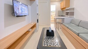 A modern living room with a TV, a sofa, a coffee table, and a kitchen area visible through an open door. - Simply And Cozy 2Br Apartment At Parahyangan Residence (Bandung)