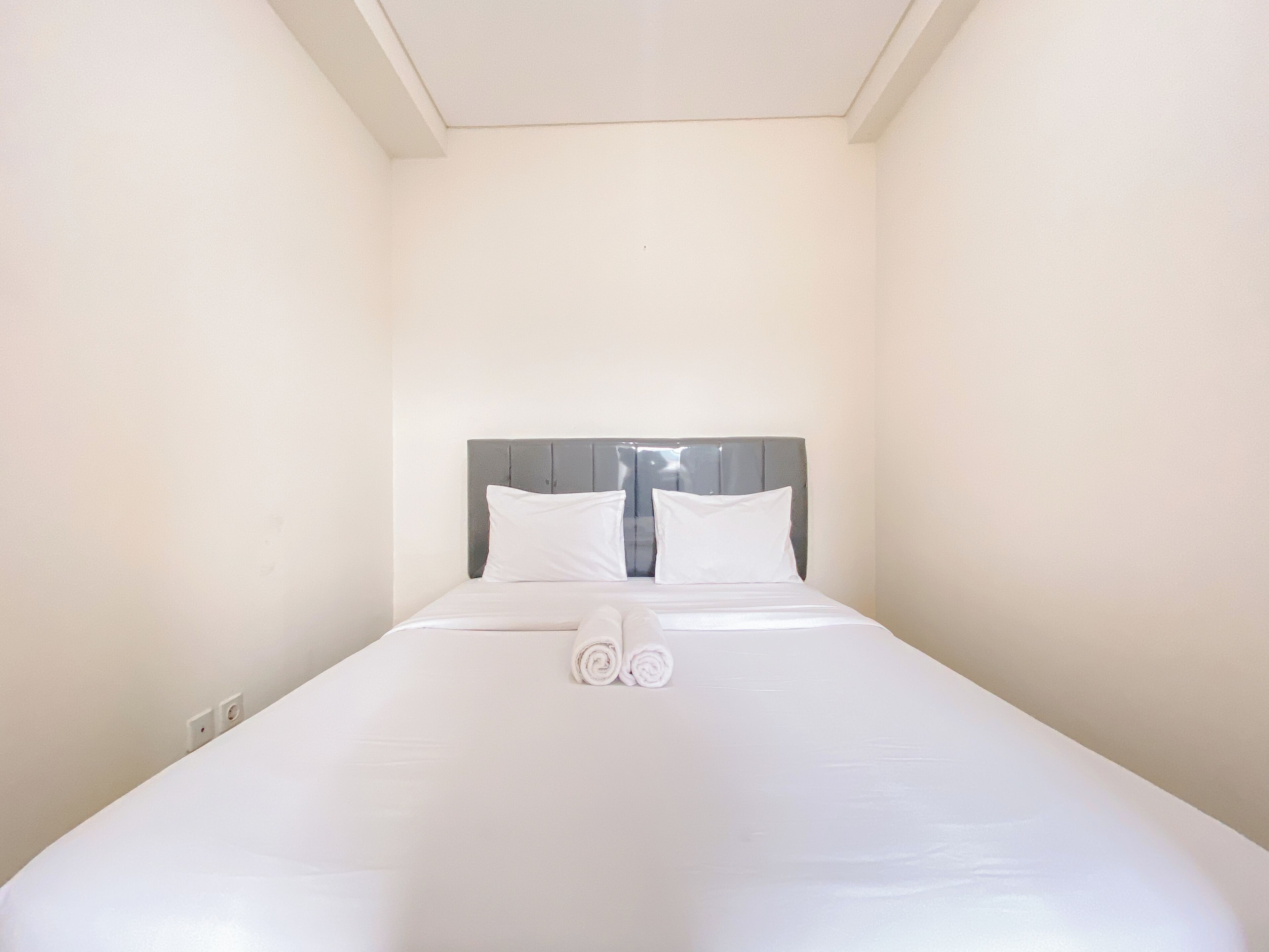 Ein ordentlich bezogenes Bett mit weißen Leinen und Kissen, ein grauer Kopfteil und ein zusammengerolltes Handtuch auf dem Bett.
