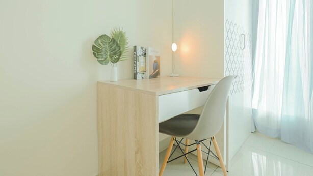Een moderne werkruimte met een houten bureau, een witte stoel, een potplant en een hanglamp.