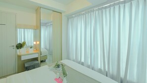 Habitación de hotel con cama, mesita de noche con lámpara, espejo y ventana con cortinas.