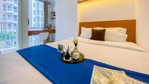 A hotel room with a bed, a desk, and a window with a view of buildings. - Relaxing and Comfortable Studio at Tokyo Riverside PIK 2 Apartment  (Teluknaga)