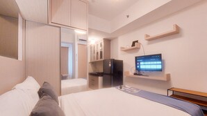 A hotel room with a bed, a TV, a refrigerator, and a wooden wardrobe.
