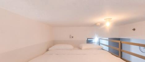 Et lille værelse med en enkelt seng, en trægavl og en lampe monteret på væggen.