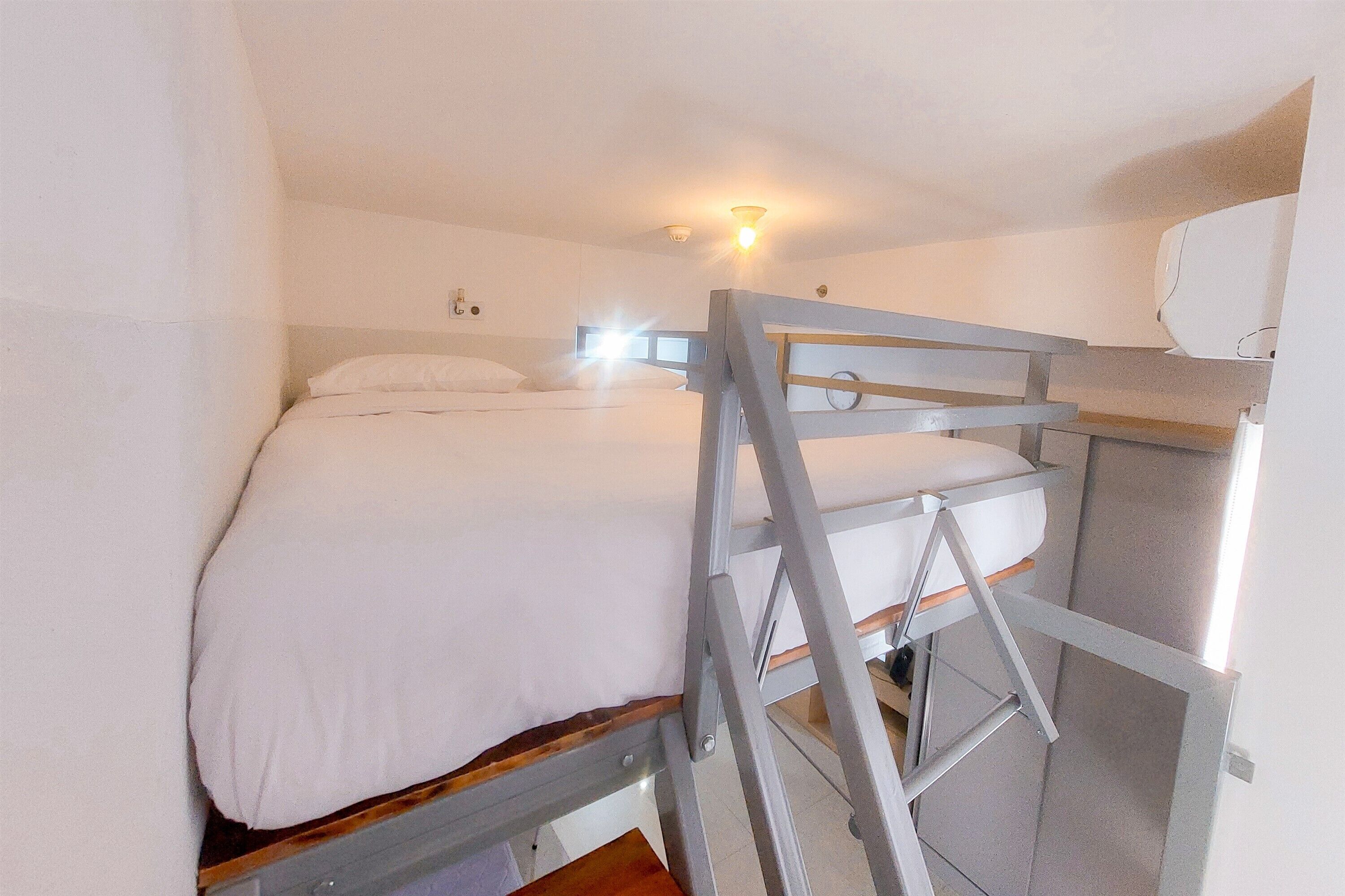 A bunk bed with a ladder, a bedside table, and a wall-mounted light fixture.